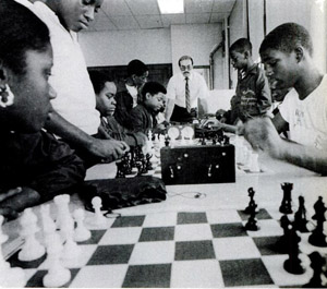 Plotting moves, the Bad Bishops are closely watched by their coach, Jeffrey Chesin (at end of table). Kevin Giles and Michael Allen  play a game of blitz (center).