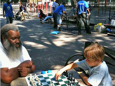 Yacahudah 'Y.A.' Harrison playing chess with a neighborhood child this summer on the table with a chessboard inlay inside Emerson Playground at Inwood Hill Park. (DNAinfo/Carla Zanoni)