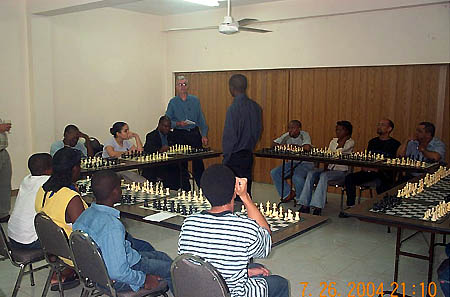 Bob Wheeler gives the participants instructions before the 15-board simultaneous exhibition begins. Jamaican Chess Federation President Ian Wilkinson (facing Simutowe) is at board #1. Copyright  2004, Daaim Shabazz.