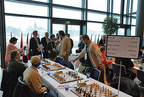 Controversy erupts in the Gabon vs. U.S. Virgin Islands match as Jean-Pierre Moulain (tan suit) protests the decision by arbiter. Michael Smith insisted on forfeit despite the fact that Moulain was present prior at the board prior to round staring. Moulain was on 8.5/10 and Smith was on 0.5/10.