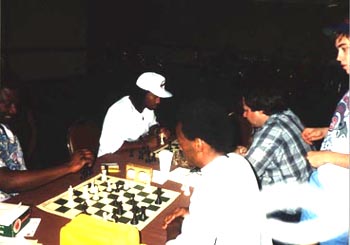 Blitz Battle! (forefront) George Umezinwa about to play Qxc8 against Allen Stewart in a blitz battle while a young Robby Adamson looks on. (background) Wallace Gordon is playing a West Coast hustler. Copyright  1989, Daaim Shabazz.