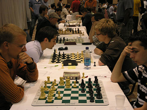 GM Viktor Laznicka vs. GM Aleksander Lenderman on the top board while GM Mesgen Amanov battles with IM Saljivus Bercys on board #2. Also on the tables are GM Jaan Ehlvest (board #3), GM Alexander Shabalov (board #4). GM Alexander Stripunsky faces GM Alexander Onischuk (board #5) and GM Surya Ganguly faces GM Nikola Sedlak (board #6).. Photo by Daaim Shabazz.